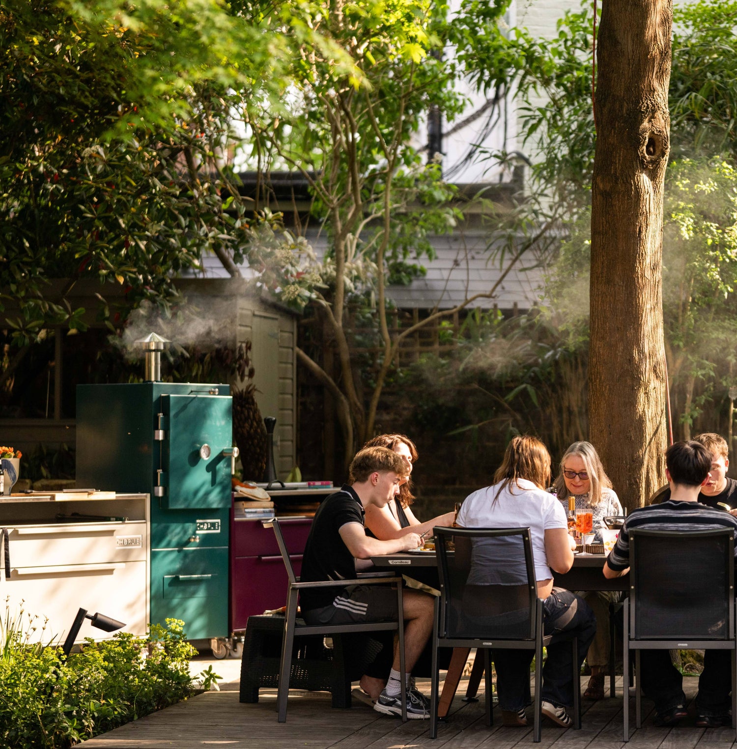 People sitting at a table in a garden setting with a barbecue in the background.
