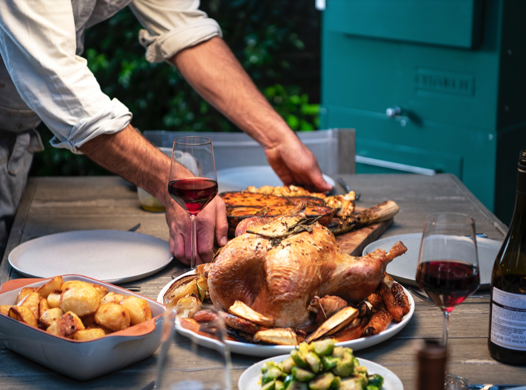 Carving a roast turkey at a garden table set for Christmas lunch, with a Charlie Oven behind