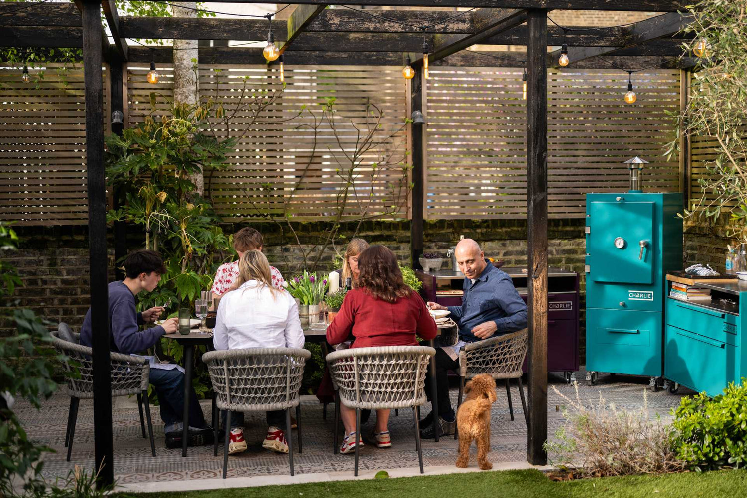 A family meal outside next to a Charlie Oven Outdoor Kitchen