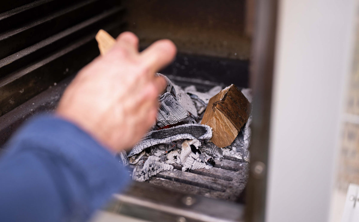 Adding a chunk of smoking wood to the hot charcoal in a Charlie Oven