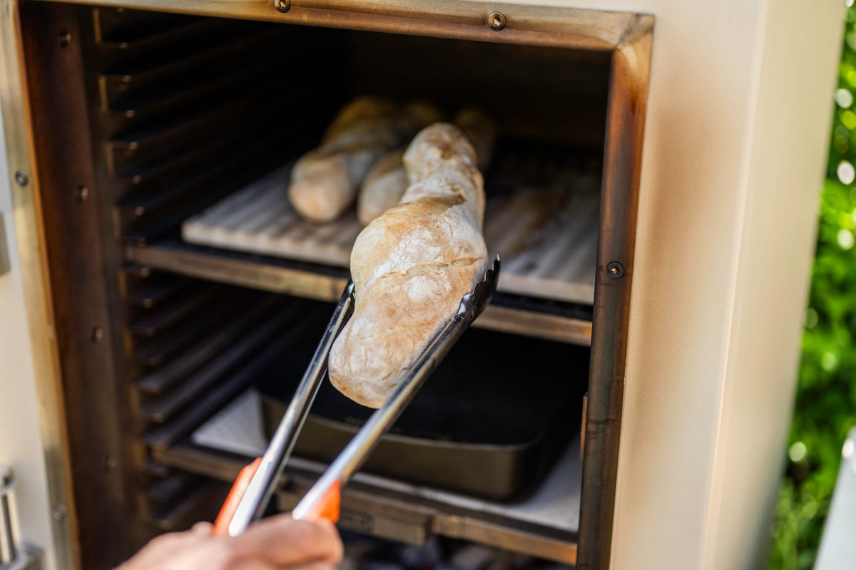 Baguettes on a baking stone on the middle level of a Charlie charcoal oven, with a tray on the level below
