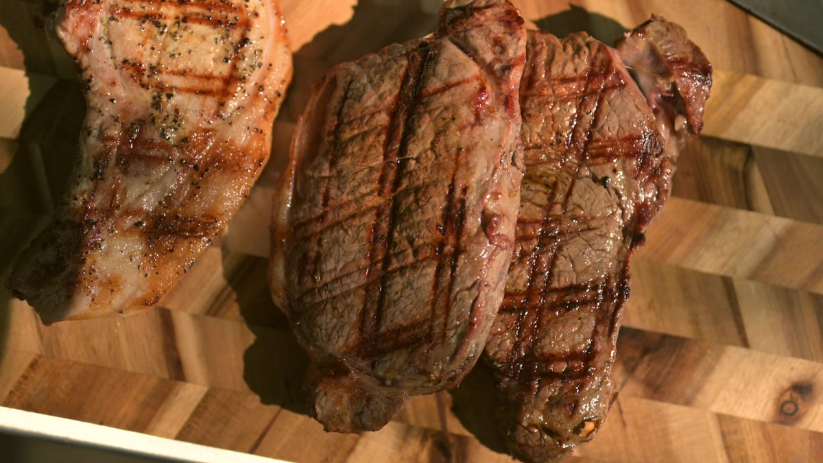 Chargrilled steaks and a pork chop resting on a board