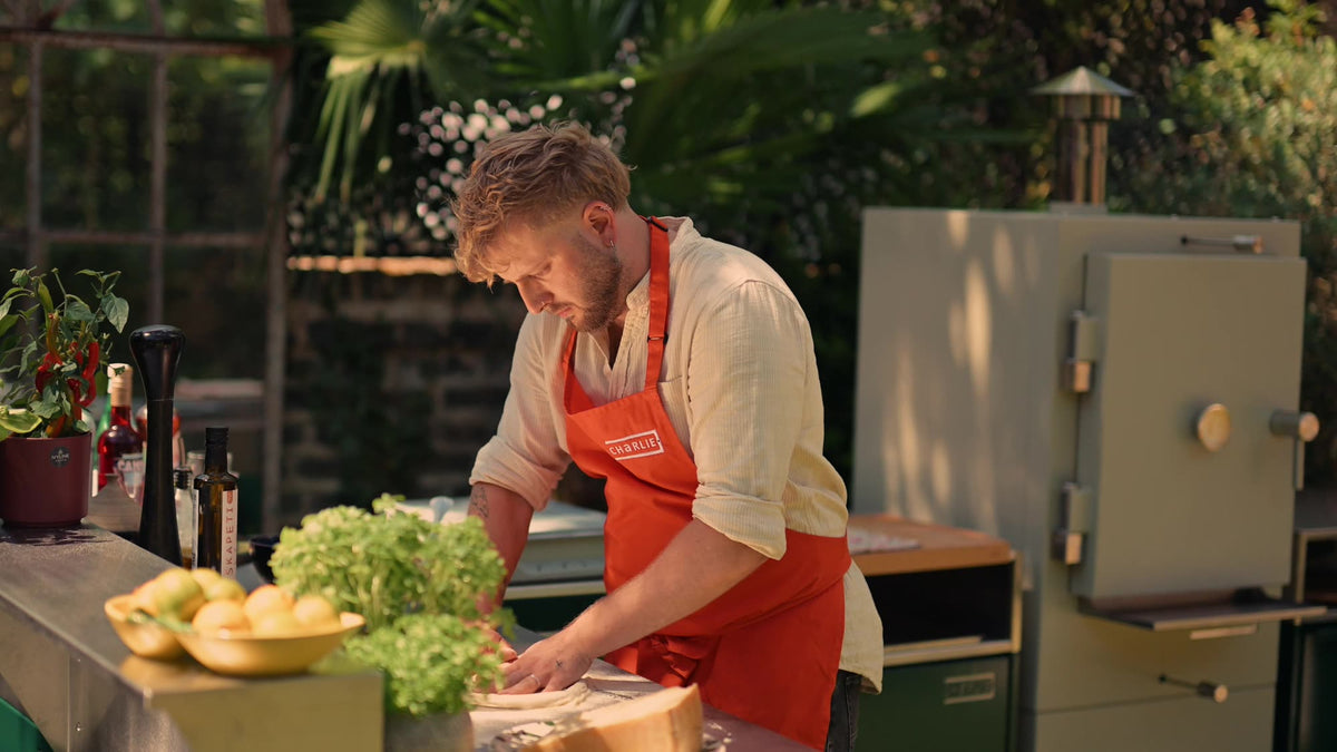 A cook preparing pizza in an outdoor kitchen beside a Charlie Oven