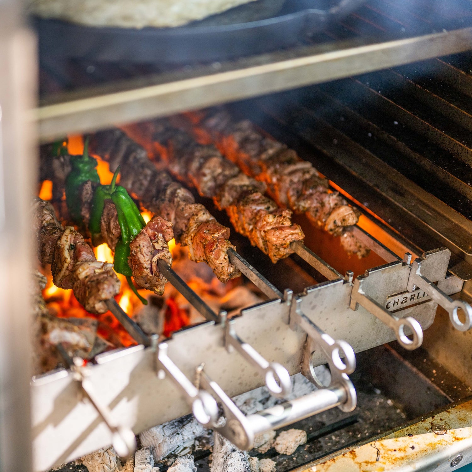 A stainless steel kebab rack with two sets of skewers cooking kebabs over an open flame grill.