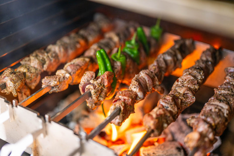 Herb-marinated lamb skewers and green peppers over charcoal flames