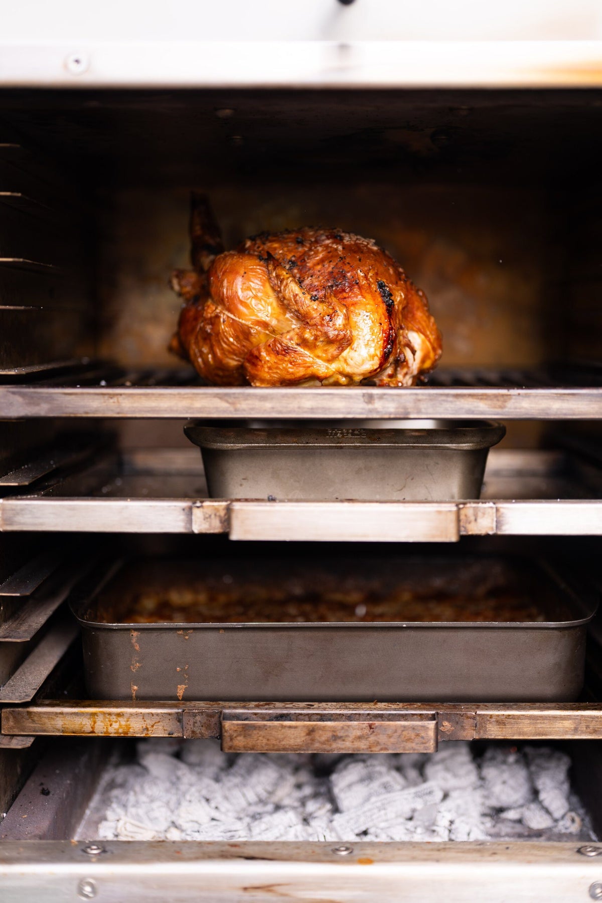 Roast chicken on the top rack, roasting tins on the levels below and charcoal glowing at the base of a Charlie Oven