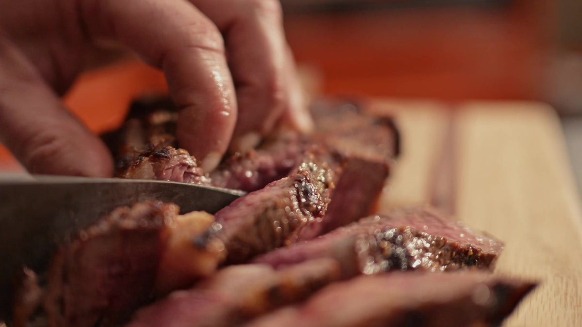 Bone-in ribeye sliced on a board, pink in the middle with a charred crust