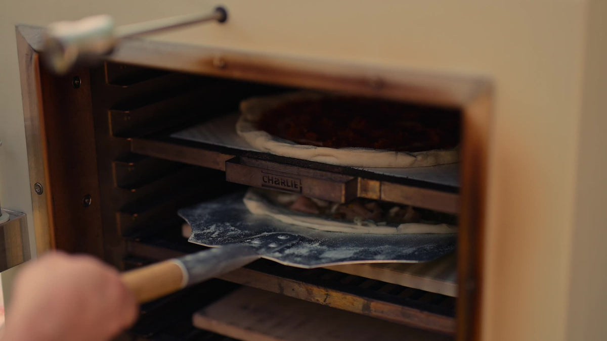 Sliding a pizza onto its stone inside the Charlie Charcoal Oven