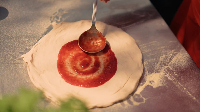 Spreading tomato sauce on pizza dough with a ladle