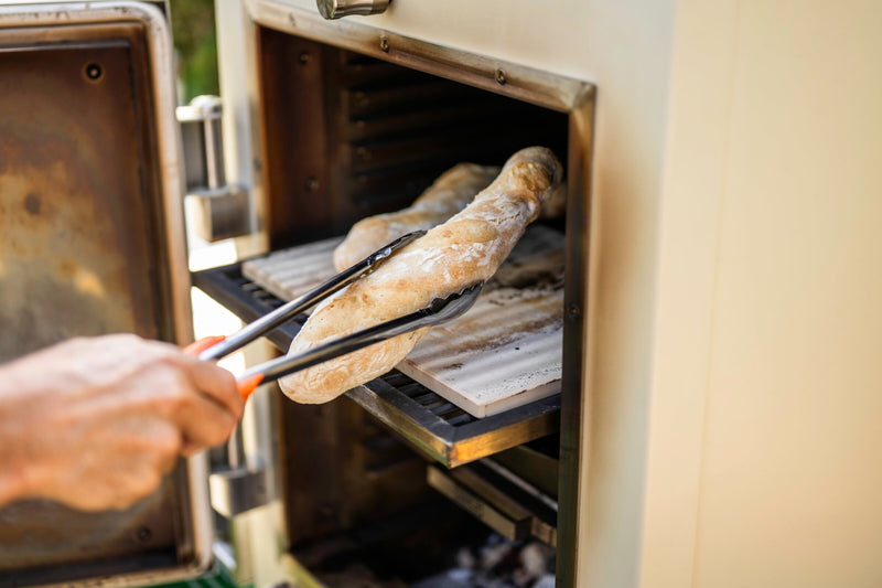 Taking a baked baguette out of a Charlie charcoal oven with tongs