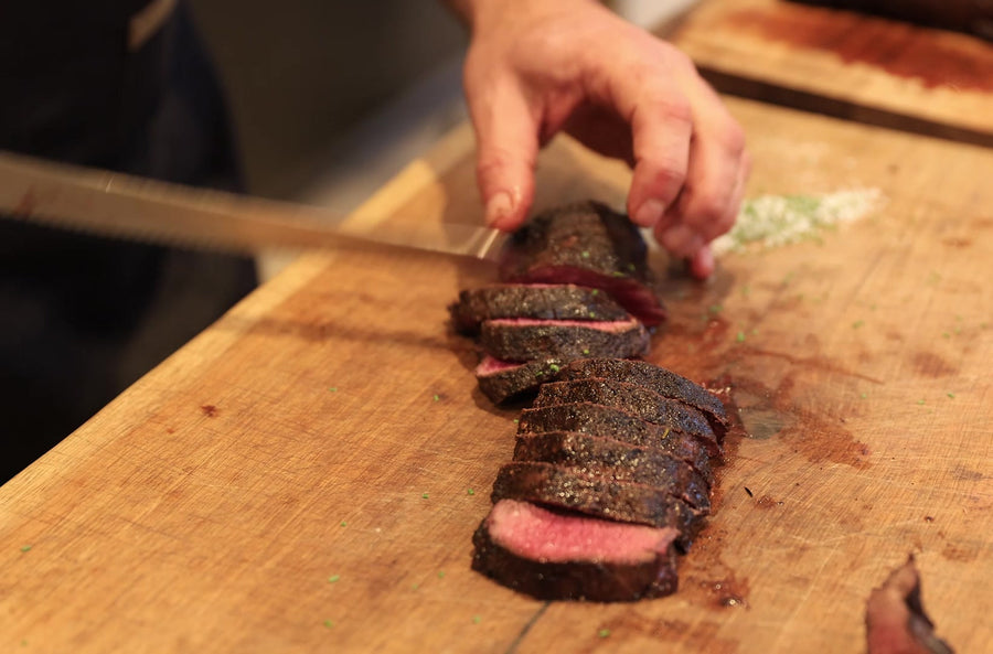Chef Chris Mackett slicing a coffee-crusted venison loin, pink in the middle, on a wooden board