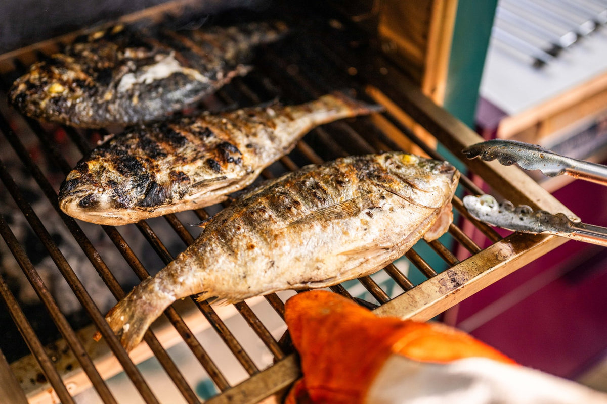 Three whole sea bream with charred skin on the grill rack of a Charlie Oven