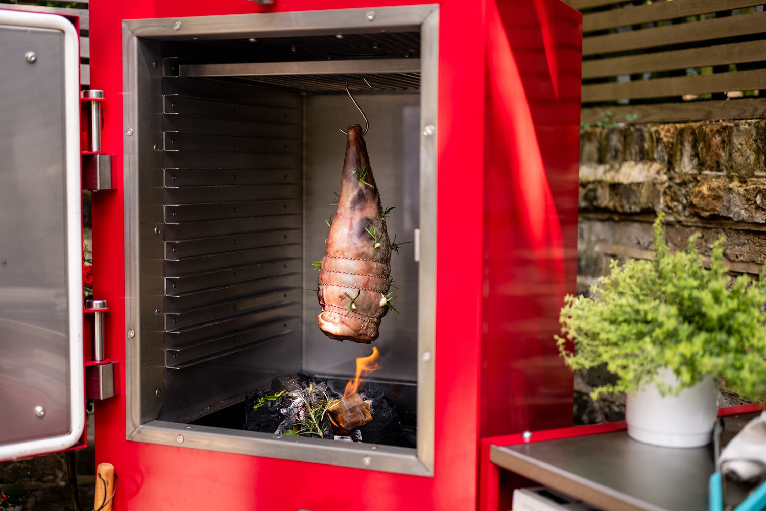 Leg of lamb hanging inside the charlie oven with a small charcoal fire with wood and bay leaves for flavour.