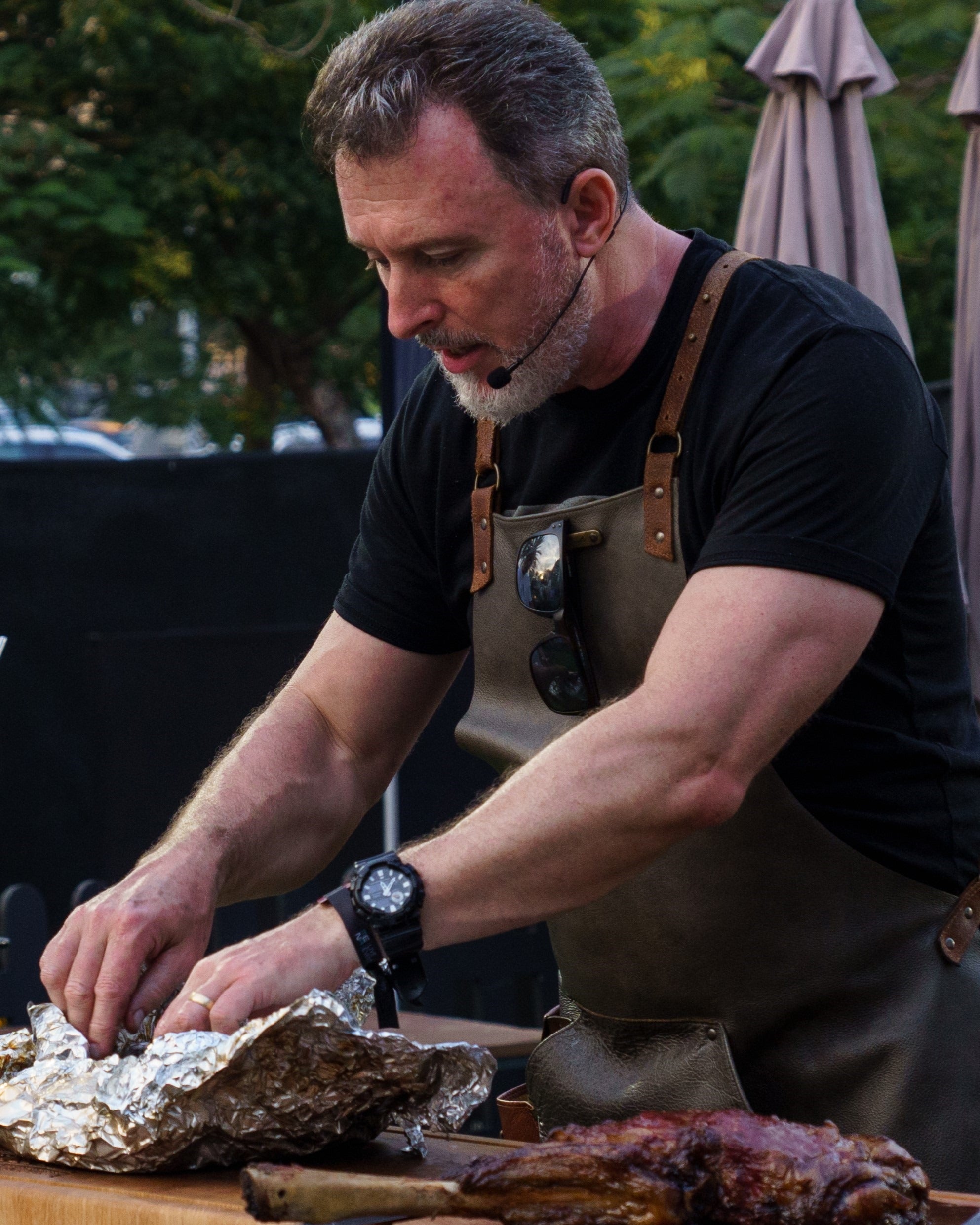 Man preparing food outdoors, wearing an apron and watch