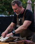 Man preparing food outdoors, wearing an apron and watch