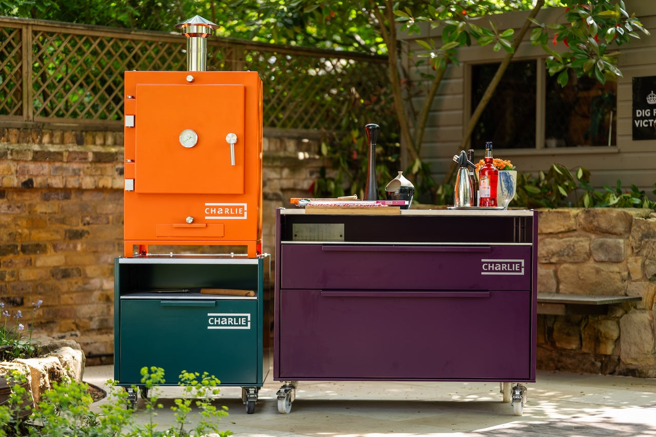 Cheeky Charlie Tabletop Oven in orange on a Charlie base cabinet beside a beetroot island unit in a garden