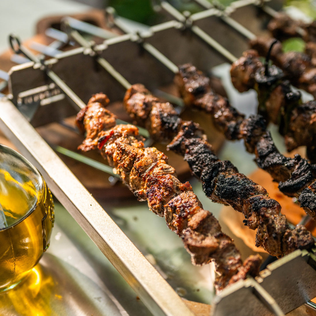 Skewers of grilled meat on a metal tray with a glass of beer.