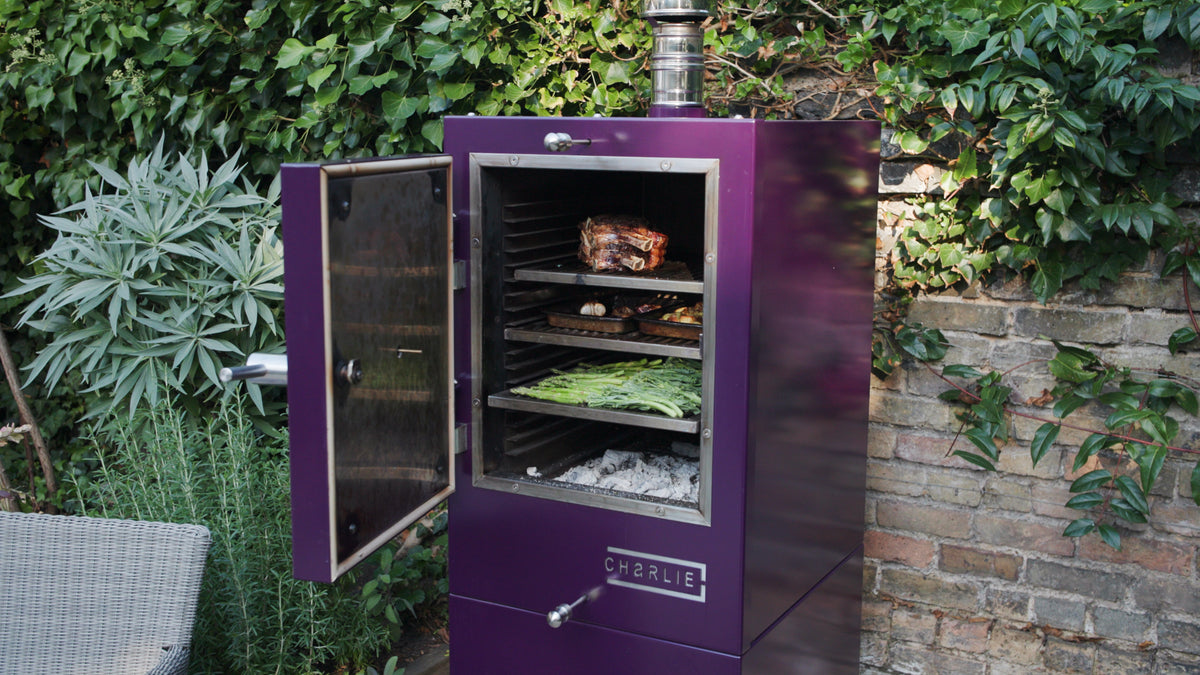 A Charlie charcoal oven in Beetroot with the door open, cooking a roast dinner on several racks at once.