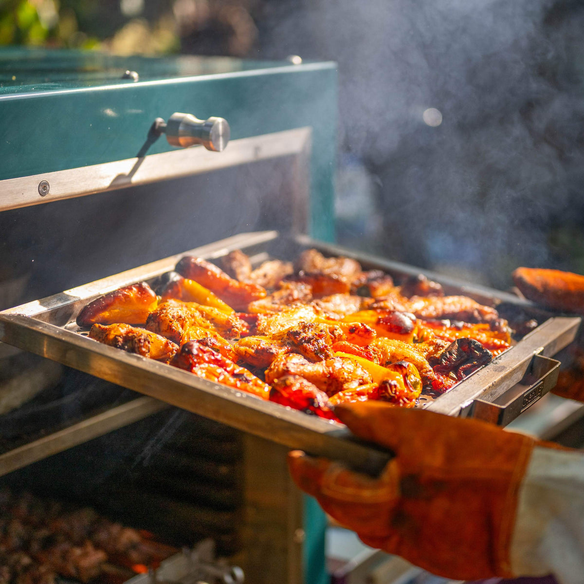 A perforated plancha tray sliding out of the front-loading door of a Charlie Charcoal Oven