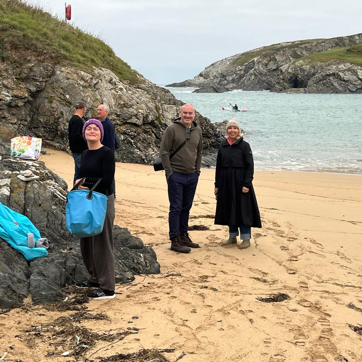 Group of people standing on a beach with rocky cliffs and clear water in the background.