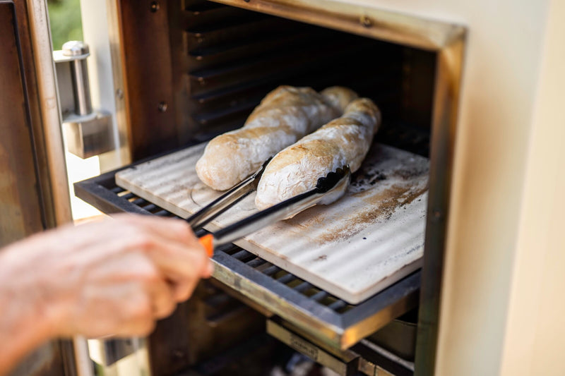 Placing baguettes on a hot Pizza and Baking Stone in a Charlie charcoal oven with tongs