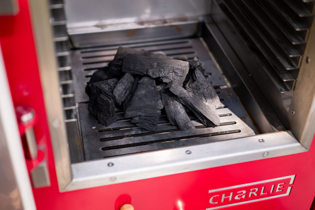 Half a football of lumpwood charcoal on the fire grates of a Charlie Oven, ready to light