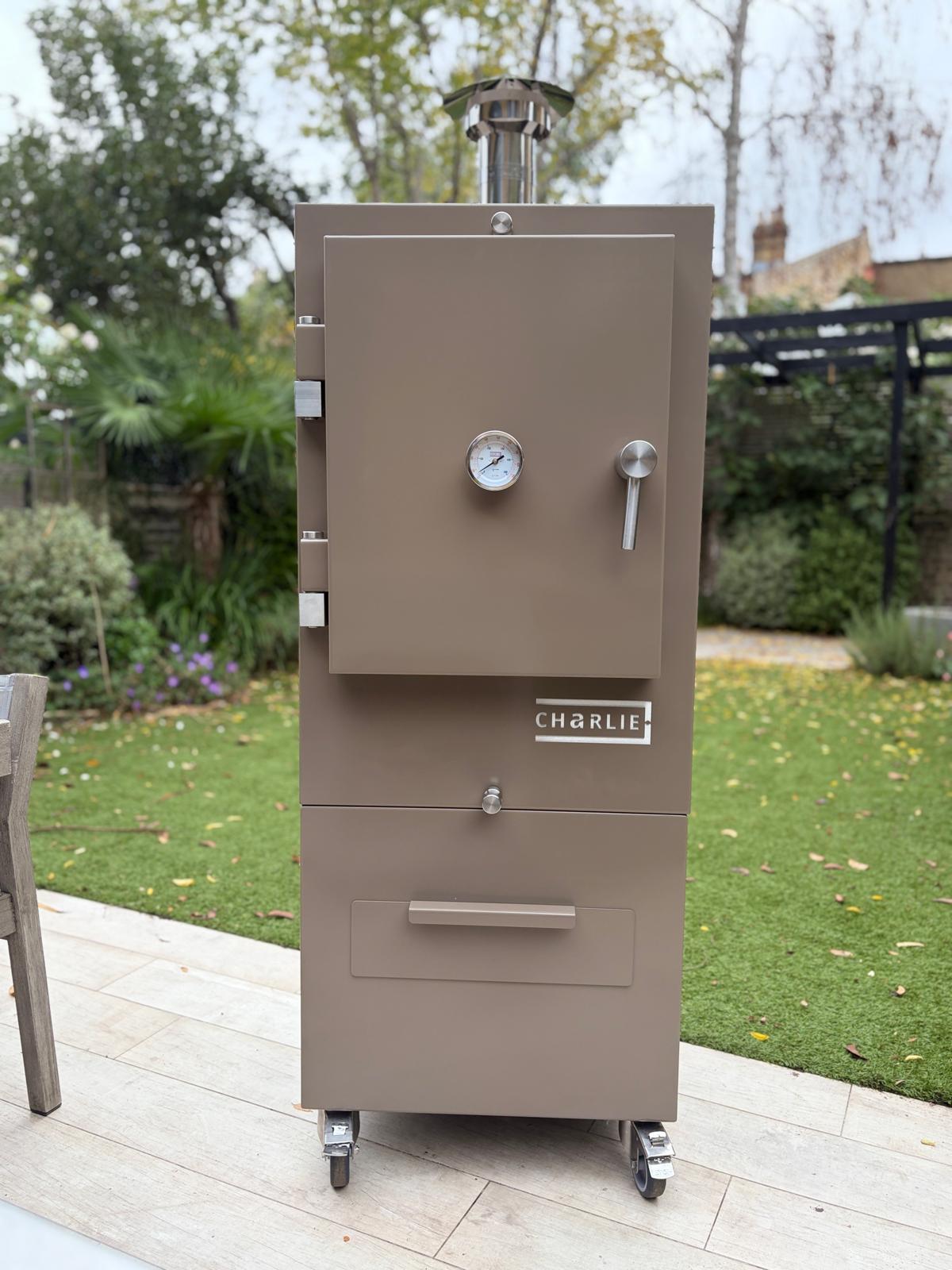 Charlie Charcoal Oven in nutmeg, a taupe brown, freestanding on a garden patio, lifestyle view 