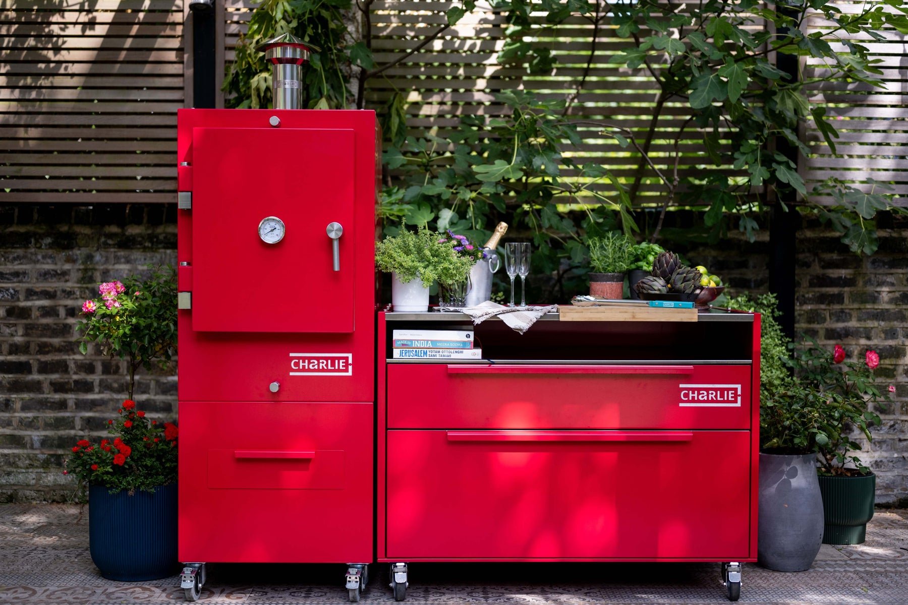 A Charlie Charcoal Oven and matching island cabinet set up in a planted garden