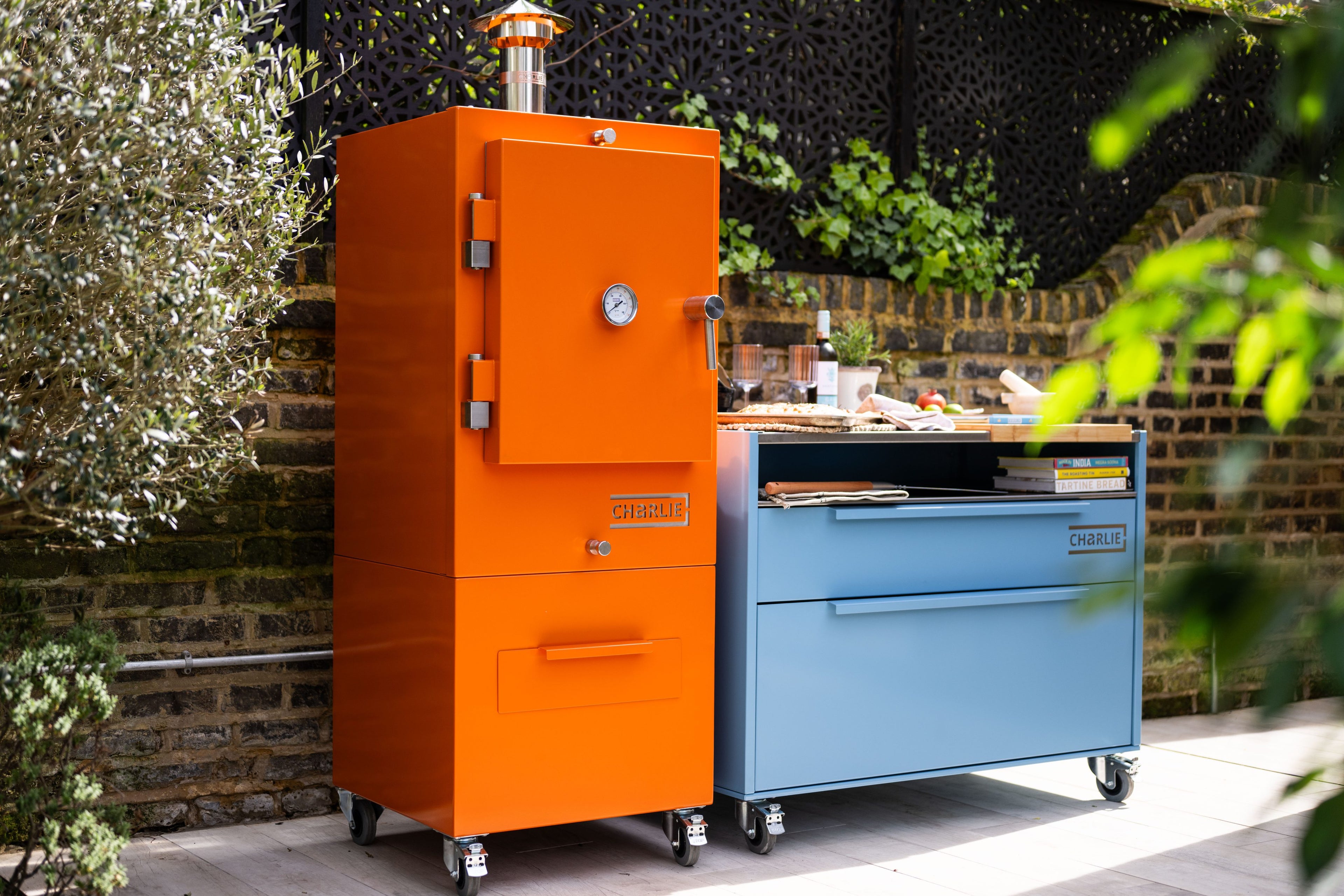 Orange Charlie Oven and blue cabinet outdoors with greenery