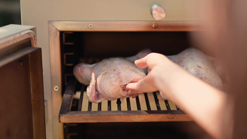 Placing a chicken on the cooking rack above the roasting tray in a Charlie charcoal oven