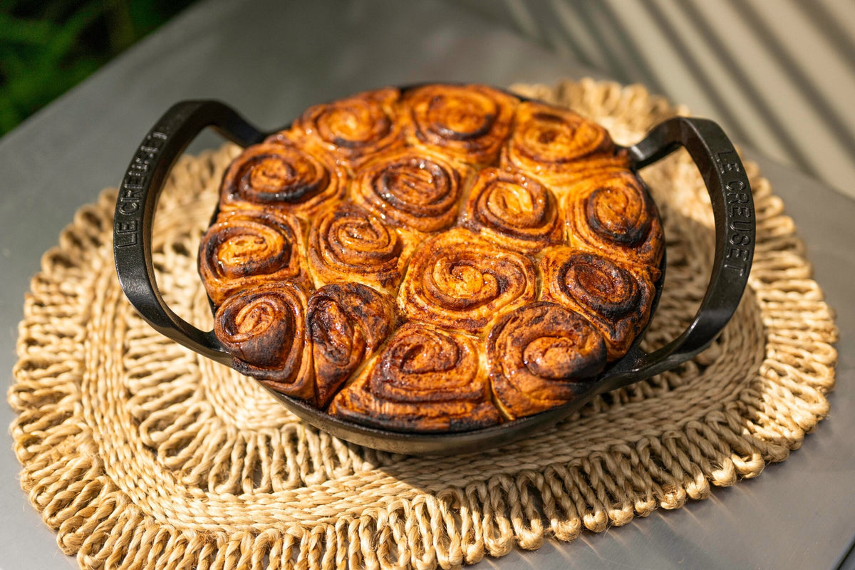 Milk bread cinnamon buns in a cast iron pan on a woven mat, fresh from a Charlie Oven