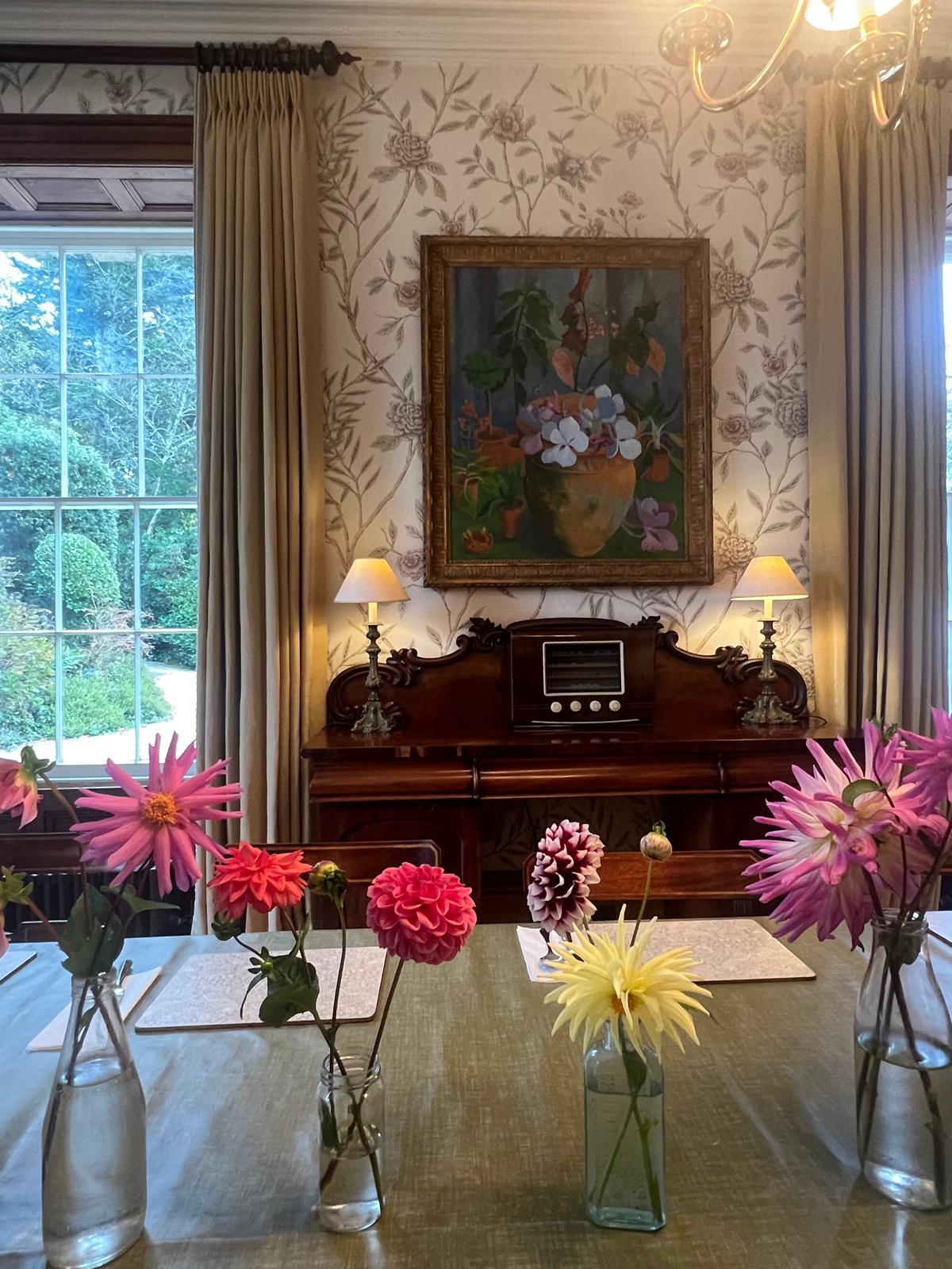Dining room with floral table setting, piano, and artwork on the wall.