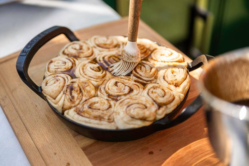Brushing cinnamon buns with butter and sugar in a cast iron pan before baking