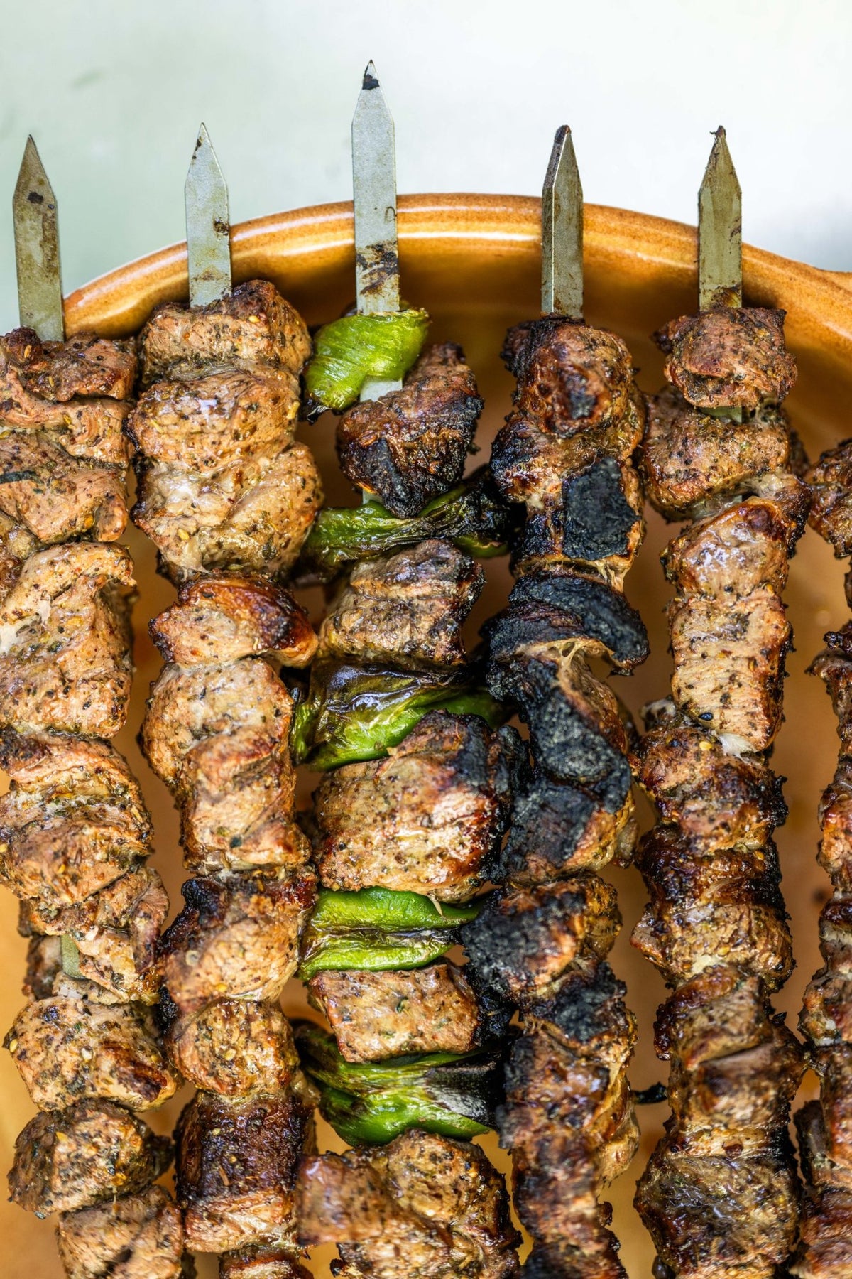 Overhead view of charred lamb and green pepper kebabs in a terracotta dish