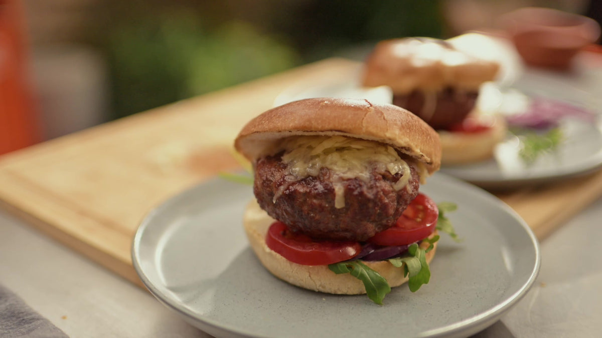 A grilled lamb burger with cheese, tomato and leaves in a brioche bun