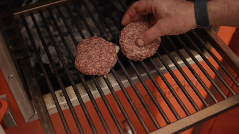 Lamb burgers placed on the grill rack above the charcoal in a Charlie Oven