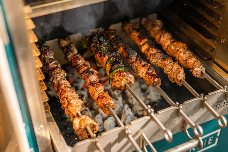 Lamb and pepper kebabs grilling over glowing charcoal on the kebab rack inside a Charlie Oven