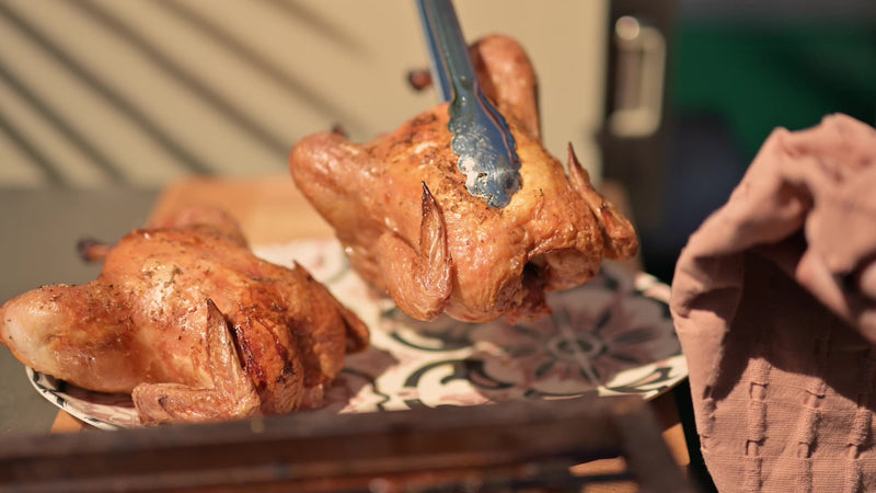 Lifting a spatchcocked roast chicken onto a platter with tongs