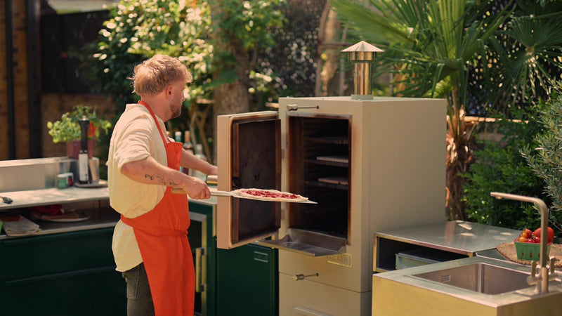 Sliding a pizza into a Charlie Charcoal Oven in a garden