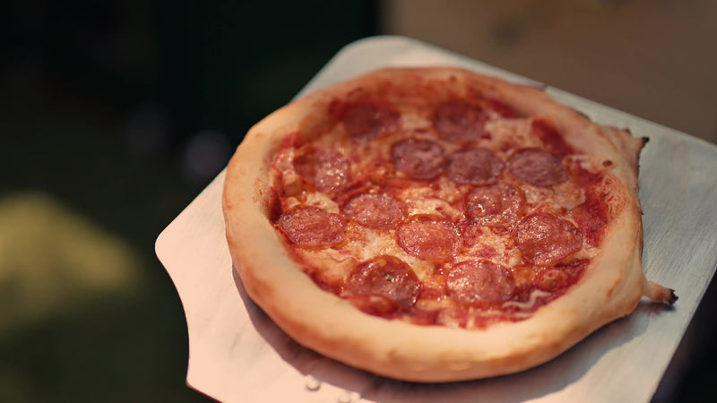 A pepperoni pizza fresh from the Charlie Charcoal Oven on a peel