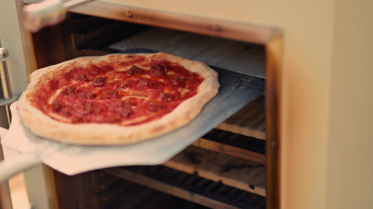 A baked pizza coming out of the Charlie Oven on a peel