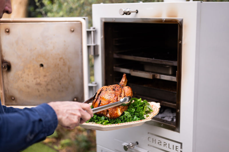 Lifting a roast chicken out of the Charlie Oven onto a platter of kale