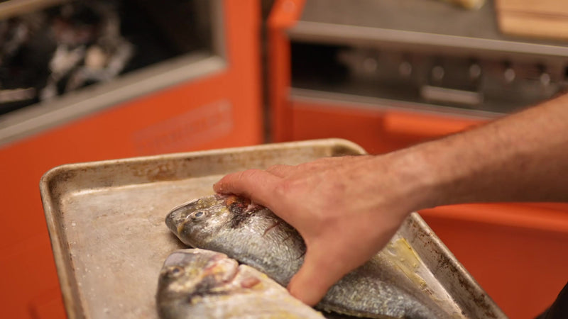 Sliding a whole sea bream onto the grill rack of a Charlie Oven