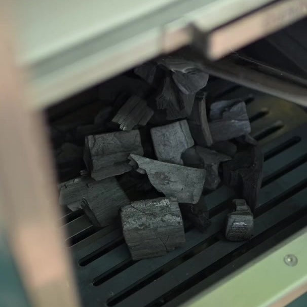 Stag British lumpwood charcoal sitting on the grates of a Charlie Oven, ready to light