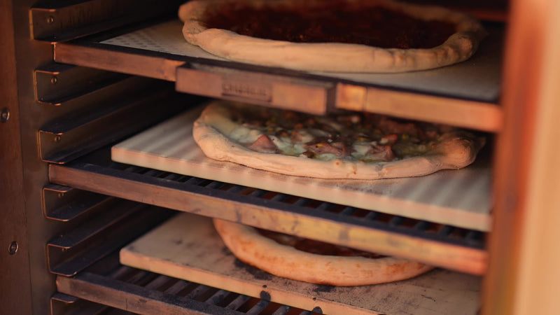 Three pizzas baking on three levels in a Charlie Charcoal Oven