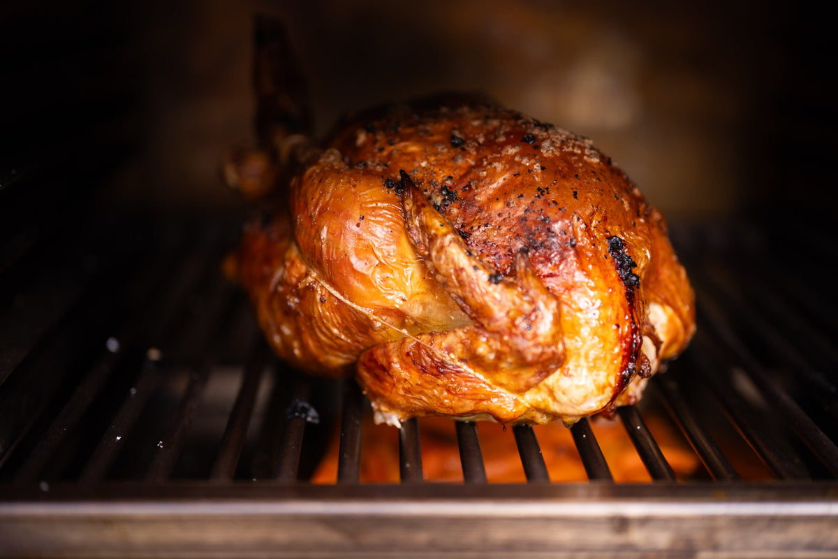 A whole roast chicken with crisp golden skin on the cooking rack of a Charlie charcoal oven